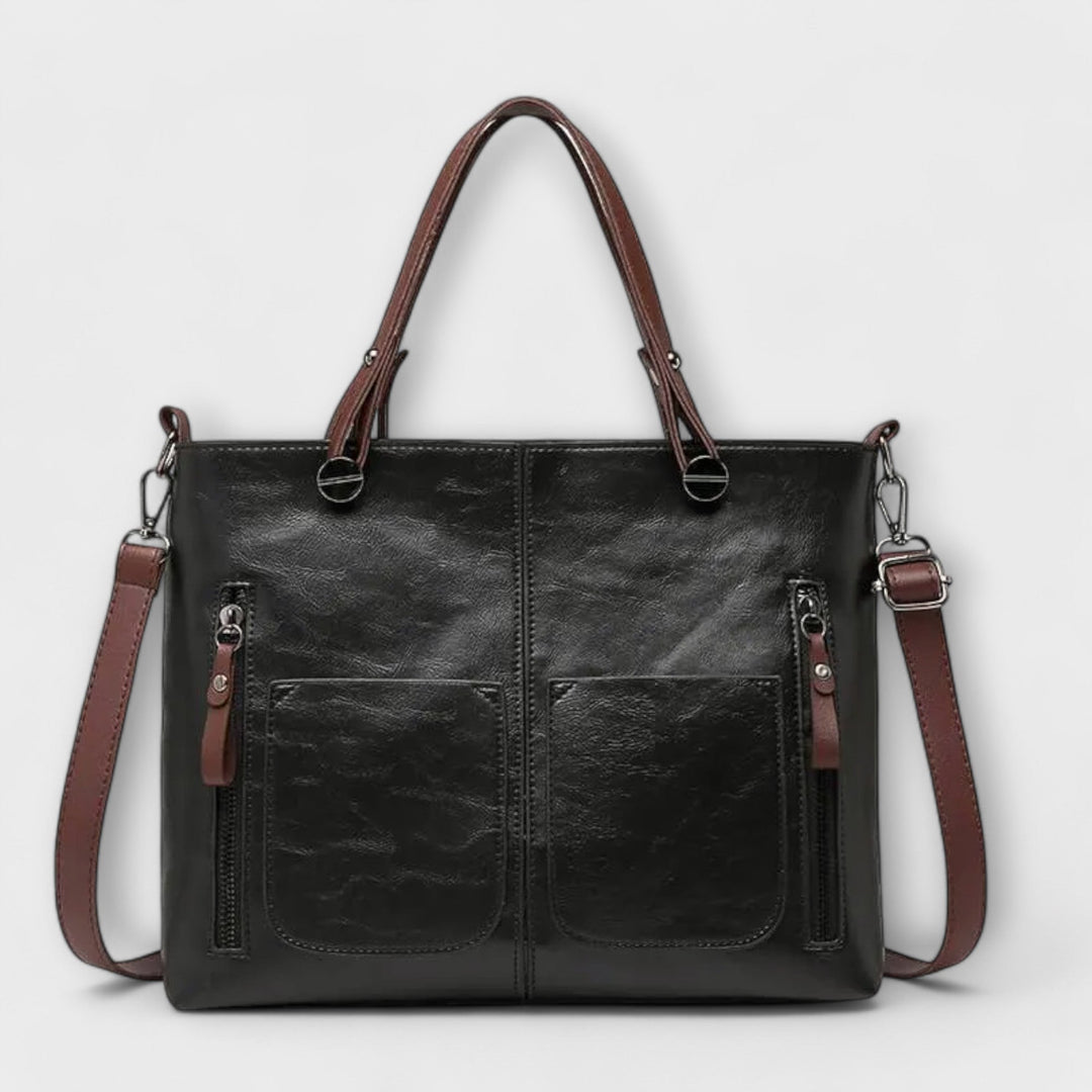Dettaglio della chiusura e dei manici robusti della borsa Cassia in pelle nera, con cuciture precise.