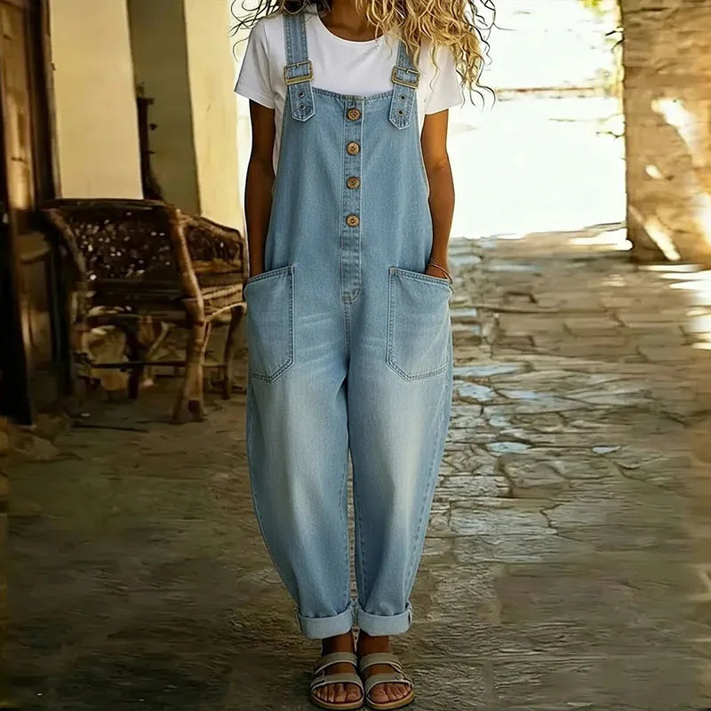 Modella che cammina all'aperto, indossando la tuta Clarissa in denim abbinata a sneakers bianche, per un look casual chic.