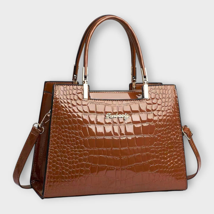 Borsa con motivo coccodrillo lucido di colore kaki, posata su una superficie elegante, vista laterale.