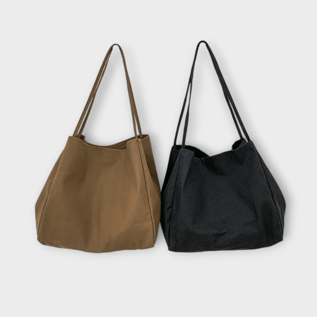 Borsa shopper in tela di colore marrone, indossata a spalla da una donna in un contesto urbano, evidenziando la sua versatilità.