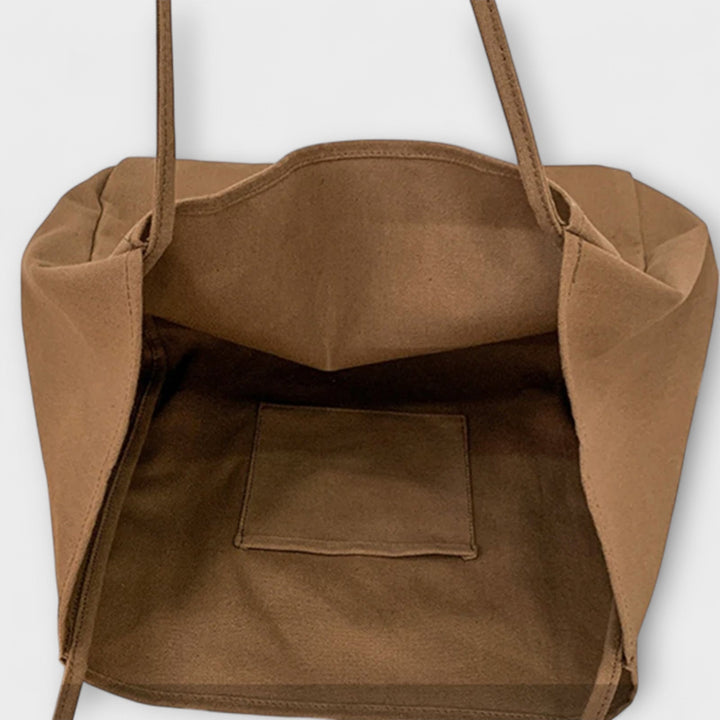 Borsa shopper in tela ampia, appoggiata su una superficie lignea, con una vista dall'alto che ne rivela le dimensioni generose e la forma.