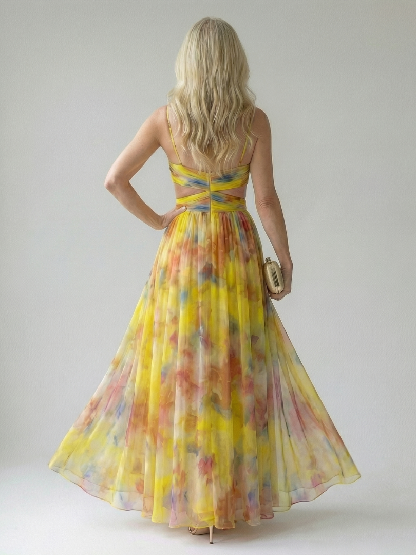 Model staand, frontaal, draagt de gele Fleur maxi wikkeljurk, met de wind die de stof licht doet wapperen.