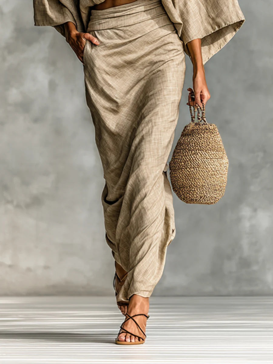 Modella in un ambiente esterno che passeggia con il completo due pezzi, mostrando il movimento elegante della gonna lunga e la vestibilità rilassata del top.