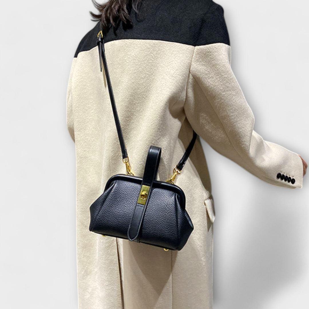 La borsa a spalla retrò nera, appoggiata su una sedia in un ambiente elegante, accentuando il suo stile.